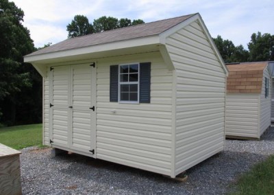 An 8x12 carriage with a shingled, carriage style roof. Shed has a shingle window with shutters and a set of double doors