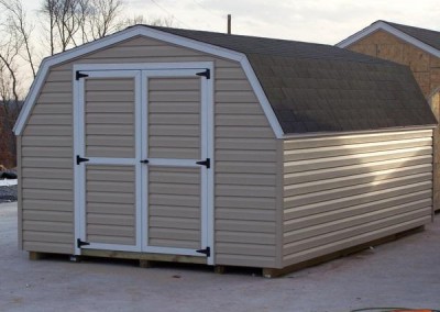 A vinyl mini barn featuring a barn styled, shingled roof with a set of double vinyl doors.