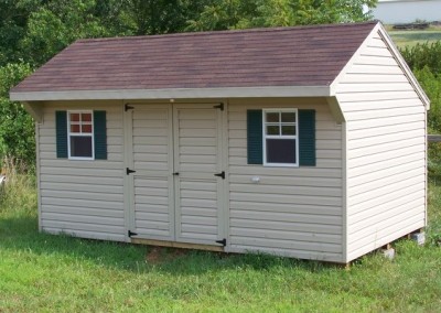 A 10x16 vinyl shed with a carriage style shingled roof. Shed has a double door and two windows with green shutters