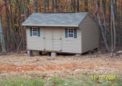 A 10x16 vinyl shed with a carriage style , shingled roof. Shed has a set of double doors and two windows with shutters