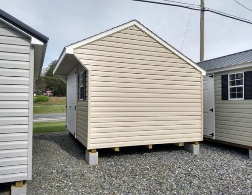 10x12 size vinyl carriage roof style shed with tan siding, white trim, black architectural shingle roof, black shutters. Has 8' ridge vent, 6 foot fiber shed doors and two windows.