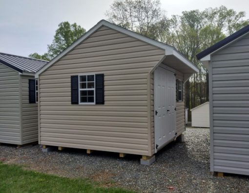 10x12 size vinyl carriage roof style shed with tan siding, white trim, black architectural shingle roof, black shutters. Has 8' ridge vent, 6 foot fiber shed doors and two windows.