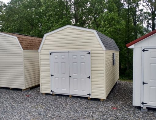 10x16 size vinyl high barn roof style shed with cream siding, white trim, estate gray architectural shingle roof, gray shutters. Has 8' ridge vent, 6 foot fiber doors and two windows.