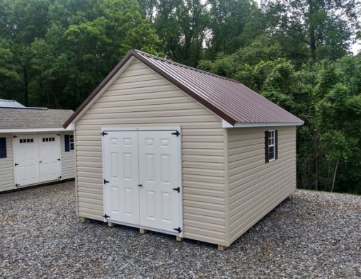 12x16 size vinyl garden roof style shed with tan siding, white trim, brown metal roof, brown shutters. Has 6 foot fiber shed doors and two windows.