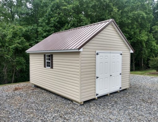 12x16 size vinyl garden roof style shed with tan siding, white trim, brown metal roof, brown shutters. Has 6 foot fiber shed doors and two windows.