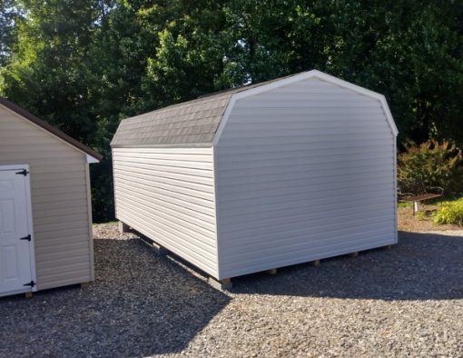 12x20 size vinyl high barn roof style shed with gray siding, white trim, black architectural shingle roof, black shutters. Has ridgevent, 6 foot fiber doors and two windows.