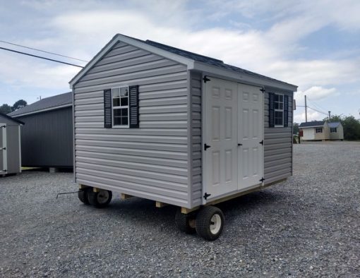 10x12 size vinyl a-roof style shed with flint siding, white trim, estate gray architectural shingle roof, black shutters. Has ridgevent, 6 foot fiber doors and two windows.