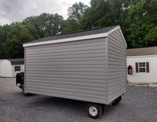 8x12 size vinyl a-roof style shed with flint siding, white trim, black architectural shingle roof, black shutters. Has ridgevent, 6 foot fiber doors and one window.