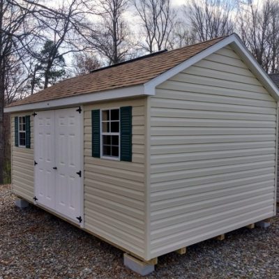 10x16 size vinyl classic roof style shed with almond siding, white trim, desert tan architectural shingle roof, green shutters. Has ridgevent, 6 foot fiber doors and two windows.