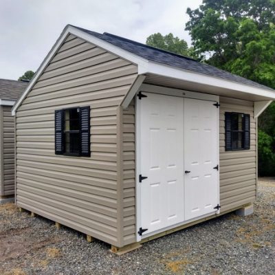 10x12 size vinyl carriage roof style shed with clay siding, white trim, black architectural shingle roof, black shutters. Has ridgevent, 6 foot fiber doors and two black windows.