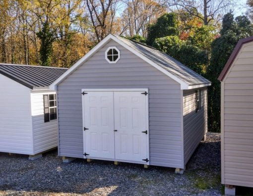 12x16 size vinyl garden roof style shed with flint siding, white trim, black architectural shingle roof, black shutters. has (1) 8' ridge vent, (1) octagon window, 6 foot fiber doors and two windows.