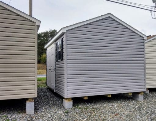 10x12 size vinyl a-roof style shed with flint siding, white trim, black architectural shingle roof, black shutters. has (1) 8' ridge vent, 6 foot fiber doors and two windows.