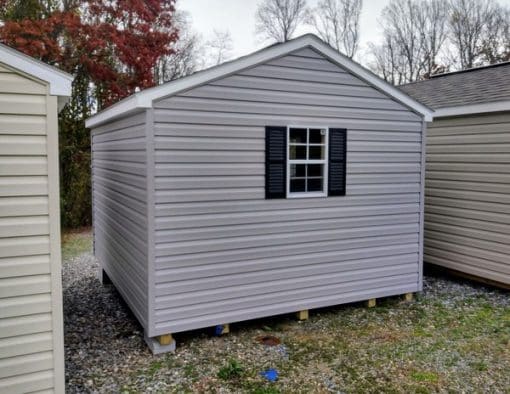 10x12 size vinyl a-roof style shed with flint siding, white trim, black architectural shingle roof, black shutters. has (1) 8' ridge vent, 6 foot fiber doors and two windows.