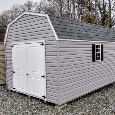 10x16 size vinyl high barn roof style shed with flint siding, white trim, black architectural shingle roof, black shutters. has (1) 8' ridge vent, 6 foot fiber 2 plank double doors and two windows.