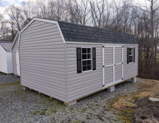 12x20 size vinyl high barn roof style shed with flint siding, white trim, black architectural shingle roof, black shutters. has (2) 8' ridge vents, ggs 6 foot double doors and two windows.