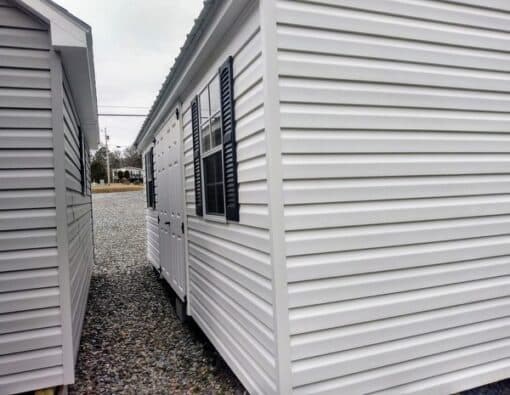 12x20 size vinyl a-roof style shed with white siding, white trim, black metal roof, black shutters. Has 6 foot fiber double doors and two windows.