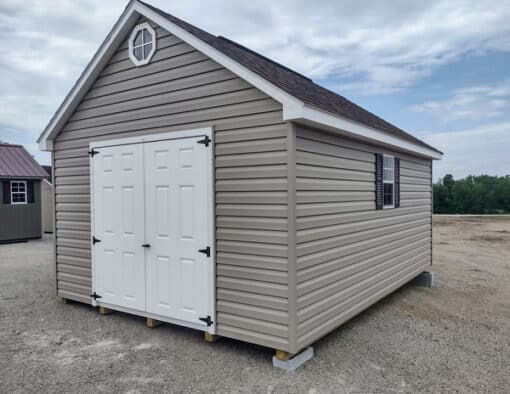 12x16 size vinyl garden roof style shed with clay siding, white trim, brownwood architectural shingle roof, brown shutters. has (1) 8' ridge vent, (1) octagon window, 6 foot fiber doors and two windows.