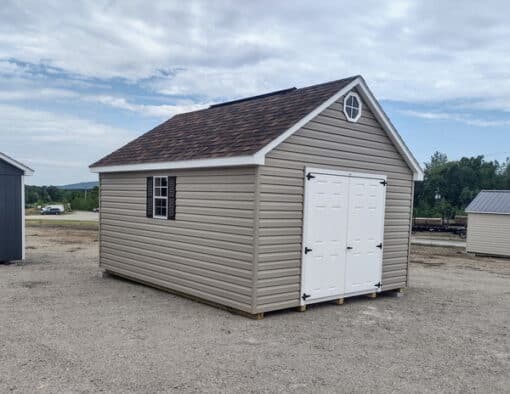 12x16 size vinyl garden roof style shed with clay siding, white trim, brownwood architectural shingle roof, brown shutters. has (1) 8' ridge vent, (1) octagon window, 6 foot fiber doors and two windows.