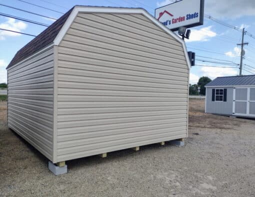 12x16 size vinyl high barn roof style shed with tan siding, white trim, brownwood architectural shingle roof, brown shutters. has 8' ridge vent, 6 foot fiber double doors and two windows.