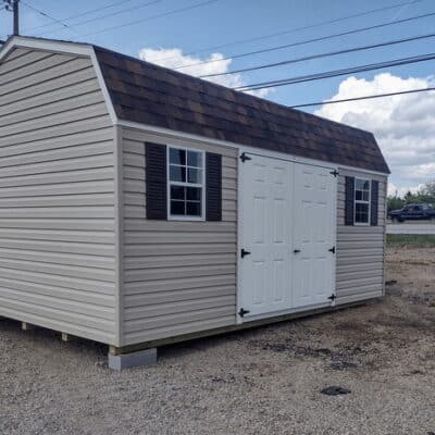 12x16 size vinyl high barn roof style shed with tan siding, white trim, brownwood architectural shingle roof, brown shutters. has 8' ridge vent, 6 foot fiber double doors and two windows.