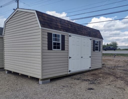 12x16 size vinyl high barn roof style shed with tan siding, white trim, brownwood architectural shingle roof, brown shutters. has 8' ridge vent, 6 foot fiber double doors and two windows.