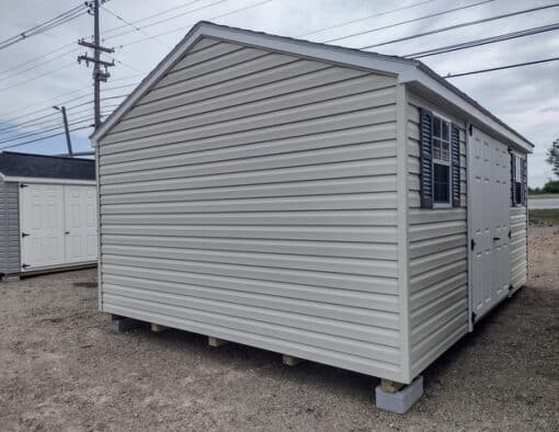 12x16 size vinyl a-roof style shed with almond siding, white trim, estate gray architectural shingle roof, gray shutters. has (1) 8' ridge vent, 6 foot fiber doors and two windows.