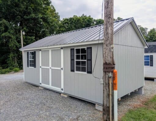 12 x 20 size painted classic style shed with gap gray siding, white trim, black metal roof, black shutters, ggs 6 foot doors, two windows.
