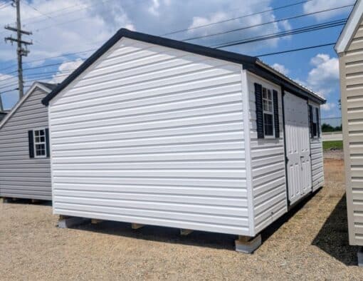 12x16 size vinyl a-roof style shed with white siding, black trim, black metal roof, black shutters. Has 6 foot fiber double doors and two windows.