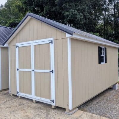 10 x 16 size painted classic style shed with tan siding, white trim, black metal roof, black shutters, ggs 6 foot double doors, two windows.