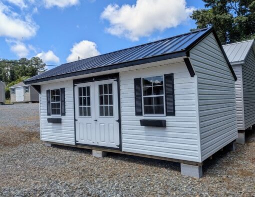 10x20 size vinyl carriage style shed with white siding, black trim, black metal roof, black shutters. Has 6 foot fiber 9 lite double doors and two windows and flower boxes.