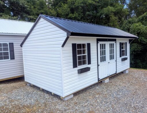 10x20 size vinyl carriage style shed with white siding, black trim, black metal roof, black shutters. Has 6 foot fiber 9 lite double doors and two windows and flower boxes.
