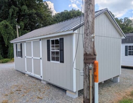 12 x 20 size painted classic style shed with gap gray siding, white trim, black metal roof, black shutters, ggs 6 foot doors, two windows.