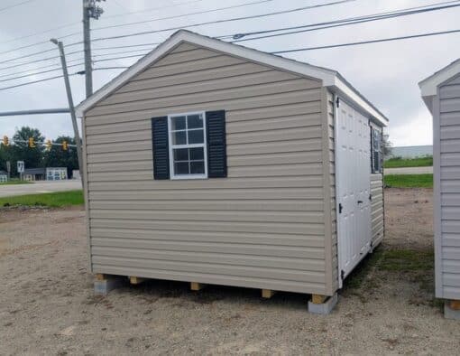 10x12 size vinyl a-roof style shed with clay siding, white trim, black architectural shingle roof, black shutters. has (1) 8' ridge vent, 6 foot fiber double doors and two windows.
