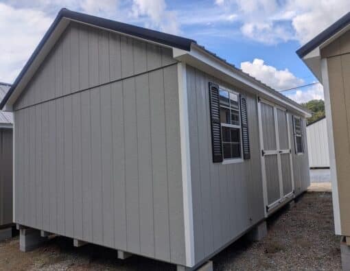 12 x 20 size painted classic style shed with gap gray siding, white trim, black metal roof, black shutters, ggs 6 foot doors, two windows.