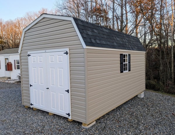 10x16 size vinyl high barn roof style shed with clay siding, white trim, black architectural shingle roof, black shutters. has 8' ridge vent, 6 foot fiber double doors and two windows.