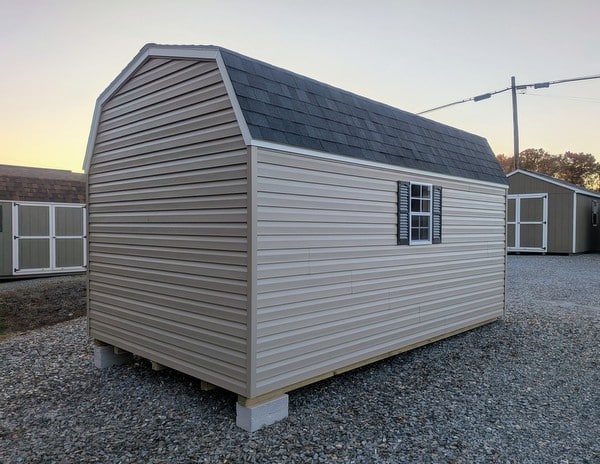10x16 size vinyl high barn roof style shed with clay siding, white trim, black architectural shingle roof, black shutters. has 8' ridge vent, 6 foot fiber double doors and two windows.