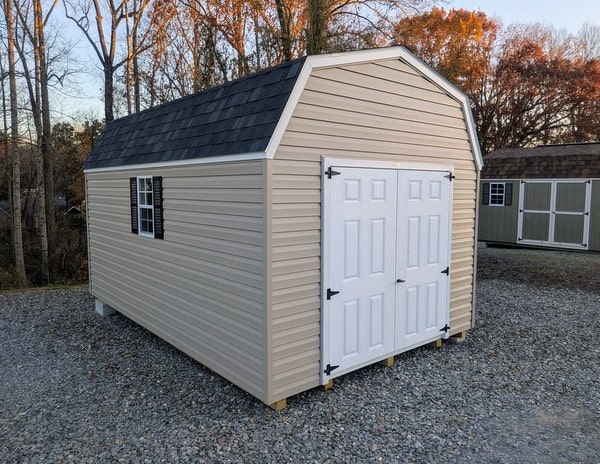10x16 size vinyl high barn roof style shed with clay siding, white trim, black architectural shingle roof, black shutters. has 8' ridge vent, 6 foot fiber double doors and two windows.