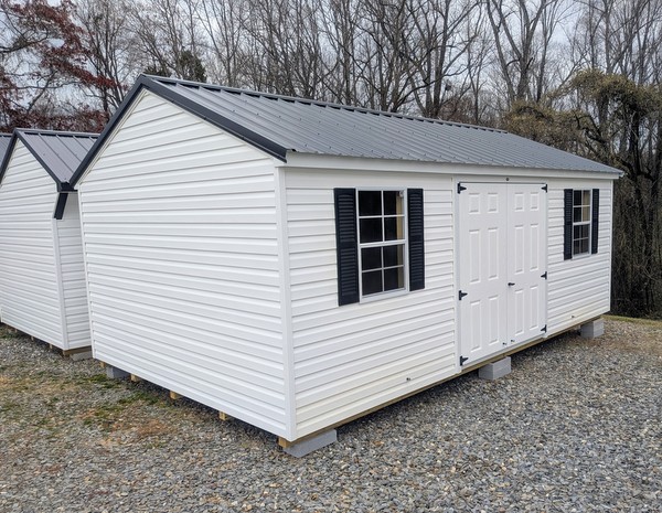 12x20 size vinyl a-roof style shed with white siding, white trim, black metal roof, black shutters. Has 6 foot fiber double doors and two windows.