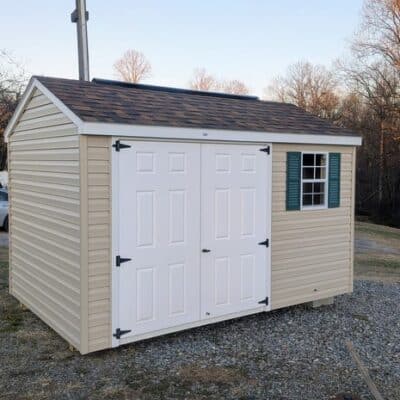 8x12 size vinyl a-roof style shed with tan siding, white trim, brownwood architectural shingle roof, green shutters. Has 8' ridge vent, 6 foot fiber double doors and one window.