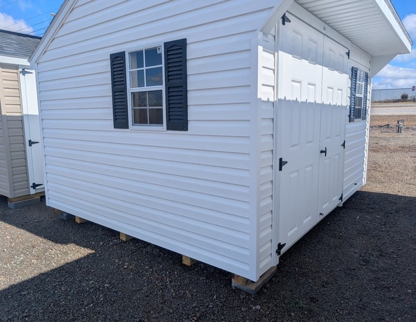 10x12 size vinyl carriage style shed with white siding, white trim, black architectural shingle roof, black shutters. has (1) 8' ridge vent, 6 foot fiber doors and two windows.