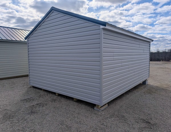 12x16 size vinyl a-roof style shed with flint siding, white trim, black metal roof, black shutters. Has 6 foot fiber double doors and two windows.