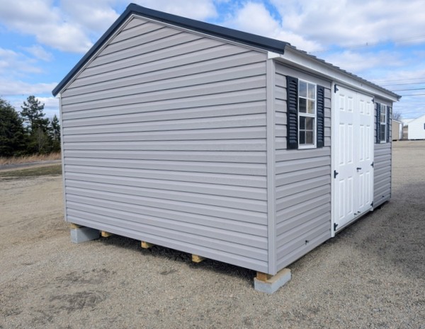 12x16 size vinyl a-roof style shed with flint siding, white trim, black metal roof, black shutters. Has 6 foot fiber double doors and two windows.