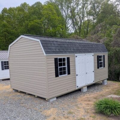 12x20 size vinyl high barn roof style shed with clay siding, white trim, black architectural shingle roof, black shutters. has (2) 8' ridge vents, fiber solid 6 foot double doors and two windows