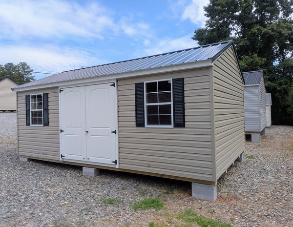 12x20 size vinyl a-roof style shed with clay siding, white trim, black metal roof, black shutters. Has 6 foot 2 plank double doors and two windows.