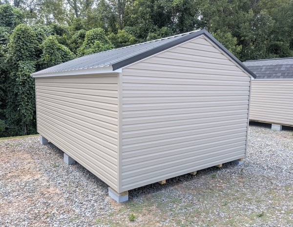12x20 size vinyl a-roof style shed with clay siding, white trim, black metal roof, black shutters. Has 6 foot 2 plank double doors and two windows.