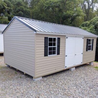 12x20 size vinyl a-roof style shed with clay siding, white trim, black metal roof, black shutters. Has 6 foot 2 plank double doors and two windows.