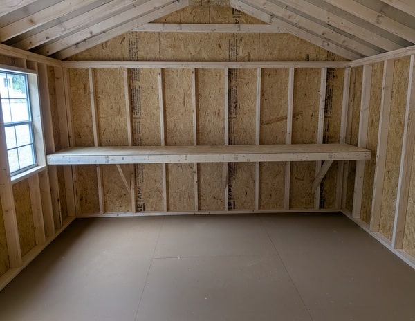 12x20 size vinyl a-roof style shed with clay siding, white trim, black metal roof, black shutters. Has 6 foot 2 plank double doors and two windows.