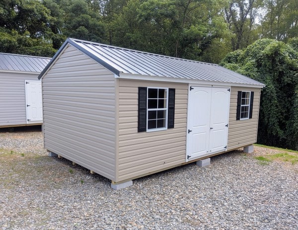 12x20 size vinyl a-roof style shed with clay siding, white trim, black metal roof, black shutters. Has 6 foot 2 plank double doors and two windows.