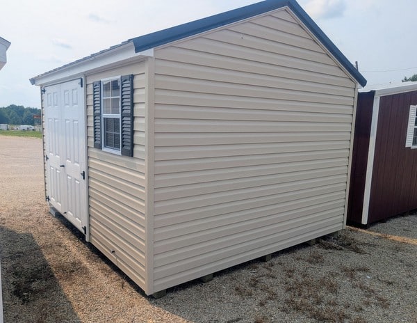 10x12 size vinyl a-roof style shed with tan siding, white trim, black metal roof, black shutters. has 6 foot fiber double doors and two windows.