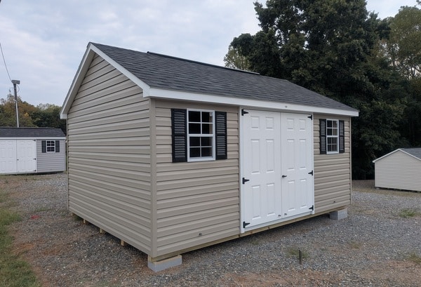 12x16 size vinyl classic style shed with clay siding, white trim, black architectural shingle roof, black shutters. has (1) 10' ridge vent, fiber solid 6 foot double doors and two windows